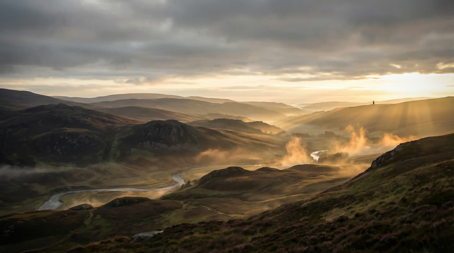 Scottish Highlands at dawn with mist rising through valleys and a distant monument silhouetted against golden light